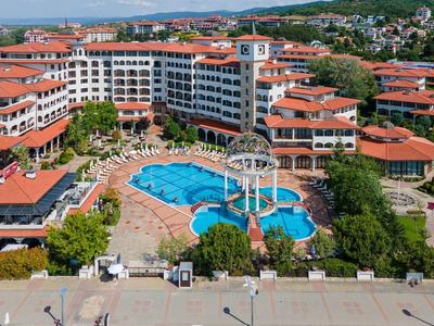 Gran hotel con piscina curva, toboganes de agua y rodeado de jardines verdes y techos rojos.