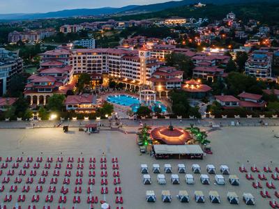 Vista nocturna de un hotel en la playa con piscinas iluminadas y tumbonas ordenadas en la arena.