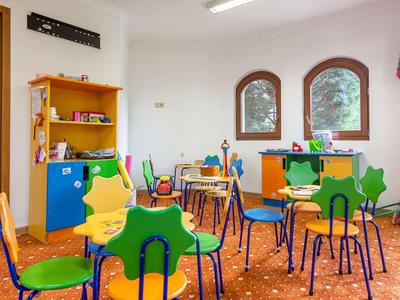 Sala infantil con sillas y mesas coloridas, juguetes y armario con libros en un hotel.