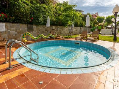 Pequeña piscina circular al aire libre con escalones, rodeada de tumbonas y sombrillas.