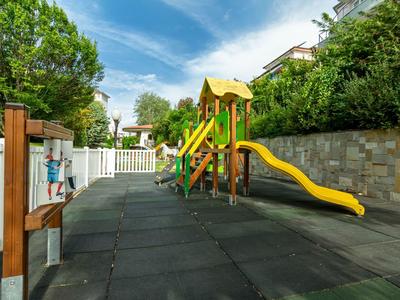Parque infantil colorido con tobogán y estructura de escalada junto a una cerca blanca bajo cielo soleado.