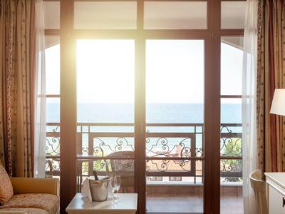 Balcón soleado con vista al mar, área de descanso y lámpara en la habitación del hotel.