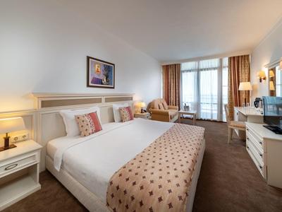 Habitación de hotel acogedora con cama doble, zona de estar, escritorio y acceso al balcón con luz natural.