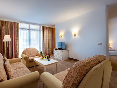 Habitación de hotel acogedora con sofá, sillones, TV y dormitorio contiguo.