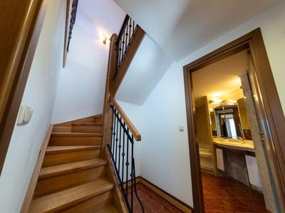 Pasillo con escalera de madera y marco de puerta abierto hacia el baño con espejo y lavabo.