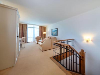 Amplia habitación de hotel luminosa con alfombra beige, sofás y balcón al fondo.