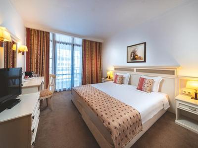 Habitación de hotel luminosa con cama doble, televisor, y balcón con cortinas marrones.