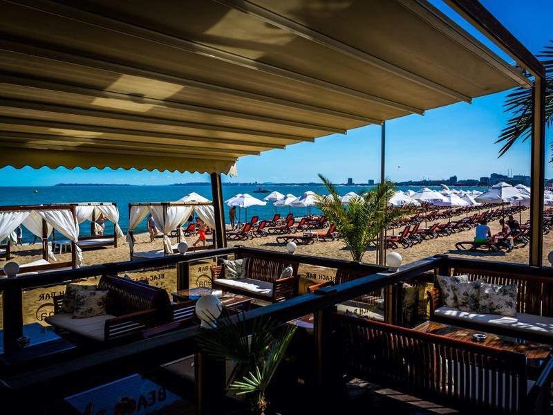 Bar de playa soleada con vista a tumbonas y sombrillas en la playa de arena.