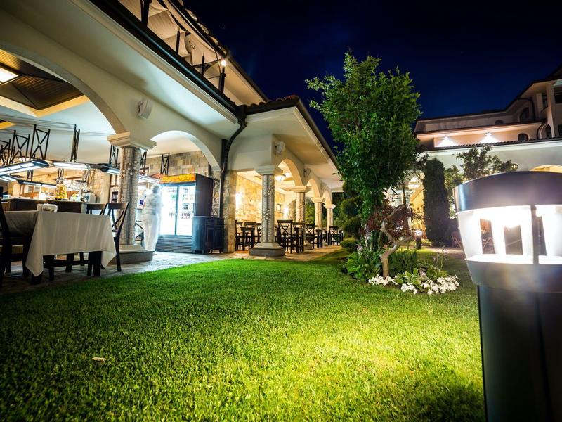 Jardín del hotel de noche con césped iluminado y áreas cubiertas para sentarse bajo un cielo despejado.