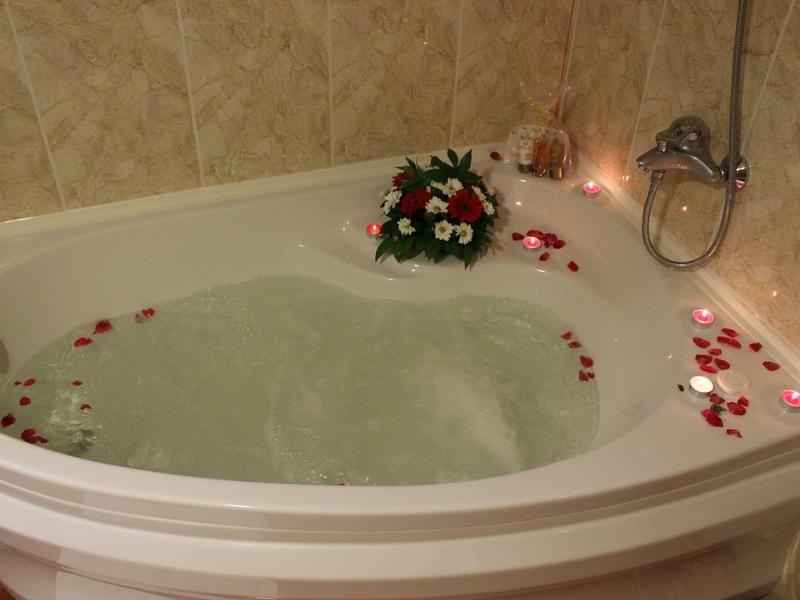 Bañera con agua, arreglo floral y velas para un ambiente romántico.