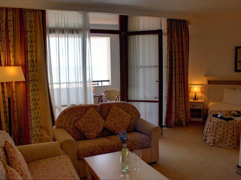 Habitación de hotel acogedora con sofá, sillón, mesa y balcón con luz natural.