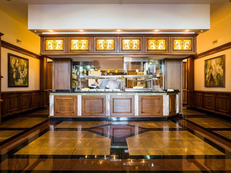 Área elegante de bar de hotel con revestimiento de madera, suelo de baldosas y barra iluminada.