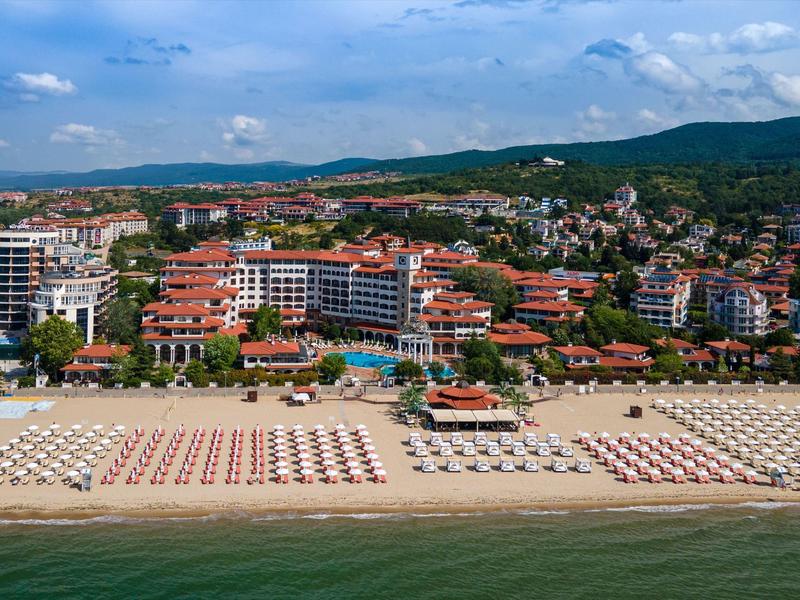 Amplia playa de arena con muchas sombrillas frente a un pueblo costero y colinas boscosas al fondo.