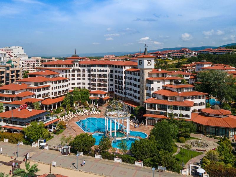 Vista de un complejo con techos rojos y una gran piscina bajo un cielo azul.