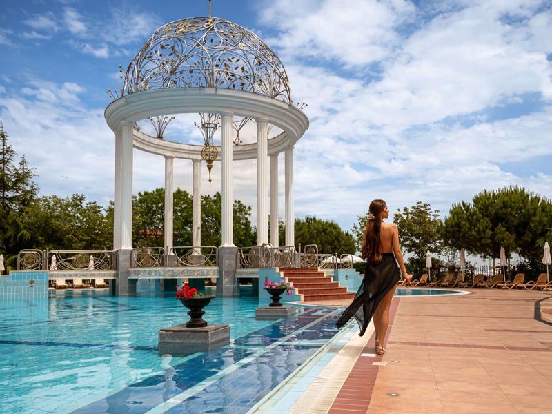 Pabellón elegante sobre una piscina amplia con plantas florecientes y cielo azul.