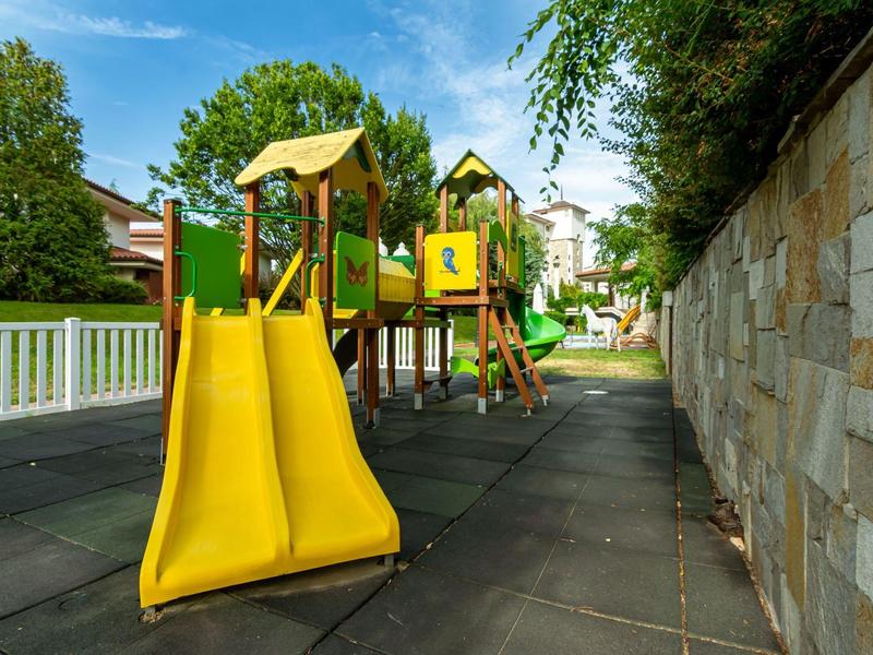 Parque infantil colorido con toboganes y estructuras para trepar en el jardín de un hotel bajo cielo azul.