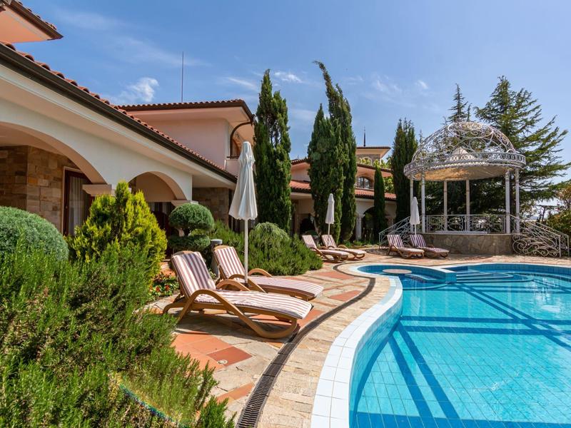 Área de piscina con tumbonas, pabellón y arquitectura mediterránea bajo cielo despejado.