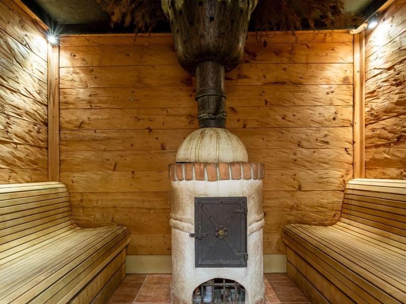 Acogedora sala de sauna con revestimiento de madera, bancos y estufa tradicional central.