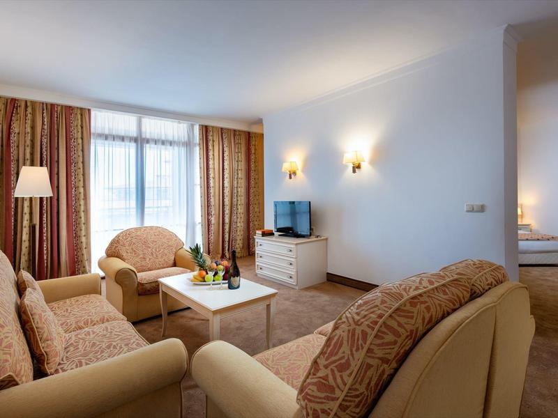 Habitación de hotel acogedora con sofá, sillones, TV y dormitorio contiguo.