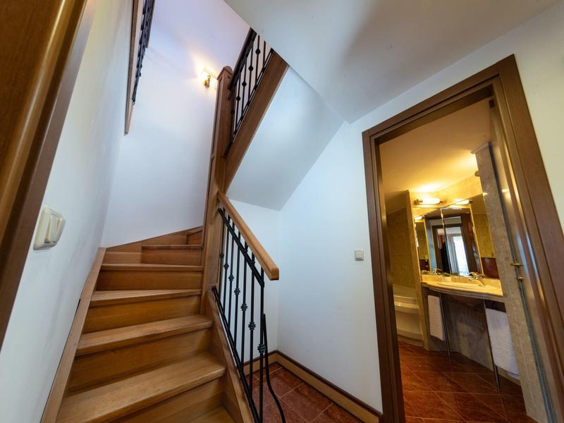 Pasillo con escalera de madera y marco de puerta abierto hacia el baño con espejo y lavabo.