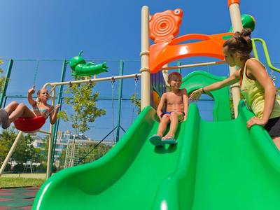 Children play on a green climbing frame with slide and swing in sunny weather.