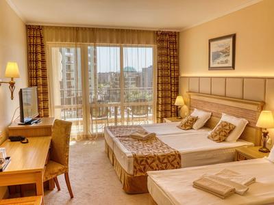 Bright hotel room with two single beds, balcony, and city view in daylight.