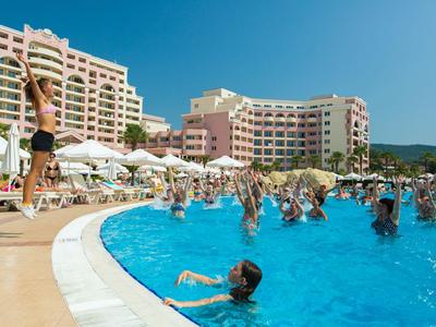 Menschen genießen den Pool und den Sonnenschein vor einem großen Hotel.