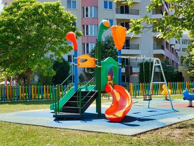 Colorful playground with slide and swing in residential area, surrounded by trees.