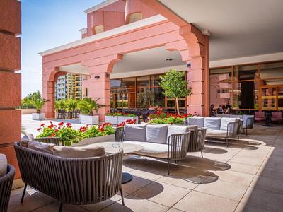Bright outdoor lounge with armchairs and sofas in front of a pink hotel building.