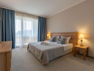 Helles Hotelzimmer mit großem Bett, blauen Vorhängen und entspannter Atmosphäre.