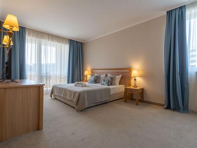 Helles Hotelzimmer mit Doppelbett, blauen Vorhängen und Holzmöbeln.