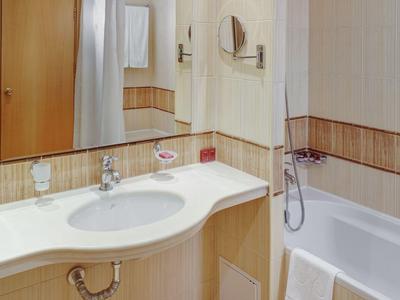 Helles Badezimmer mit Waschtisch, Spiegel und Badewanne mit Duschvorrichtung.