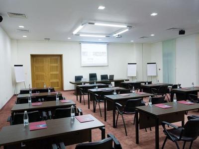 Moderner, heller Tagungsraum mit Reihen von Tischen und Stühlen, Leinwand und Flipcharts.