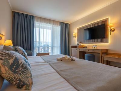Modernes Hotelzimmer mit Doppelbett, großen Fenstern und TV an der Wand.