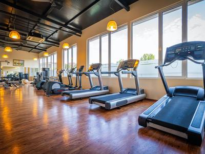 Moderner Fitnessraum mit Laufbändern und anderen Trainingsgeräten neben großen Fenstern.