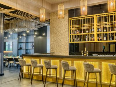 Moderner Hotelbarbereich mit gelben Akzenten, Barhockern und stilvoller Beleuchtung.