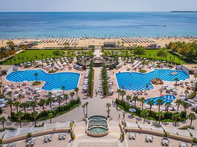 Zwei große Pools mit Liegestühlen neben einem Sandstrand und Meerblick in einer Hotelanlage.