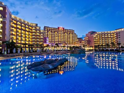 Großes Hotel mit beleuchteten Balkonen und reflektierendem Pool bei Dämmerung.