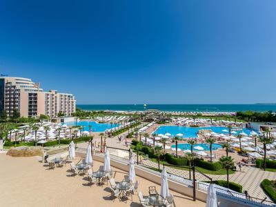 Large hotel complex with multiple pools, sun loungers, and sea view.