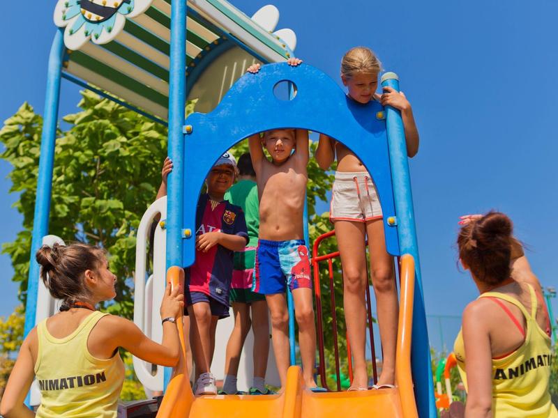 Children happily playing on a colorful outdoor slide with two supervisors.
