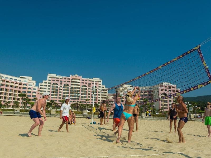 People playing volleyball on the beach in front of a hotel under clear sky.