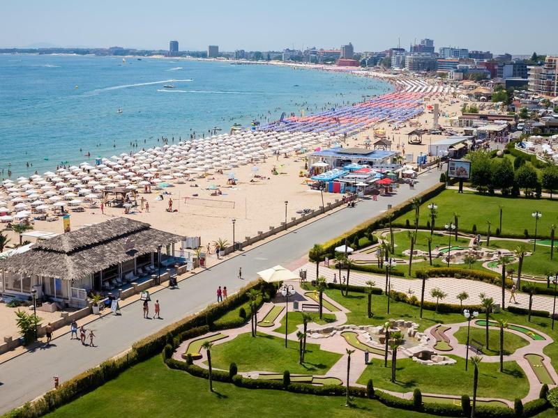 Beach with numerous umbrellas, adjacent sea, and a well-maintained mini golf course in the foreground.