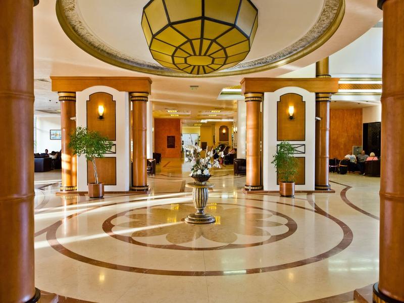 Elegant hotel lobby with marble floor, large columns, and intricate ceiling lighting.