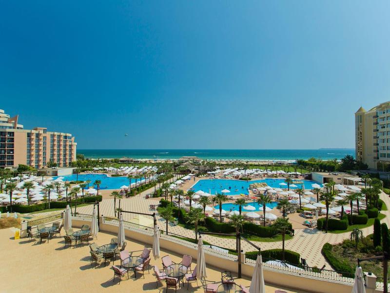 View of a large hotel pool with lounge chairs and the sea in the background on clear weather.