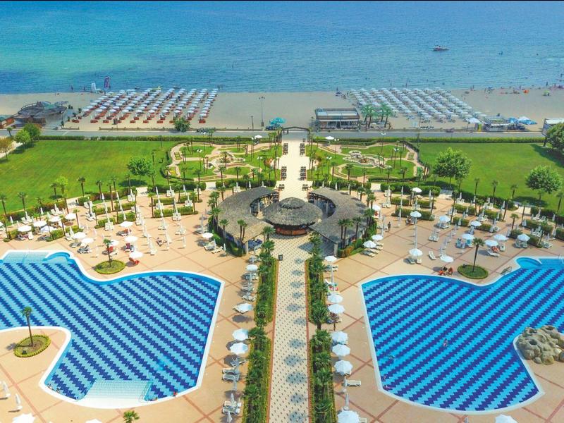 Large resort with two curved pools, sun loungers, and a view of the beach.