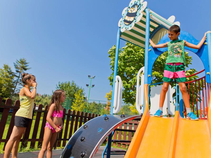Children playing on a playground slide under clear blue sky.