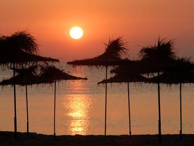 Sonnenuntergang über ruhigem Meer mit Schatten von Sonnenschirmen am Strand