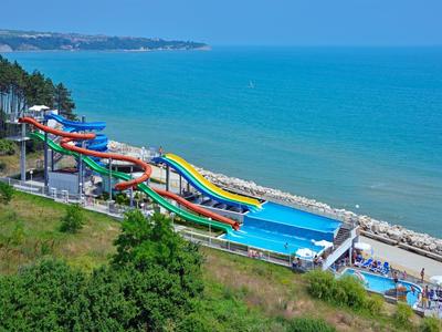 Mehrere bunte Wasserrutschen entlang der Küste mit Blick auf das blaue Meer.