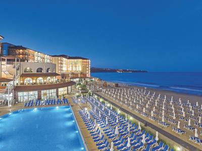 Abendansicht eines Strandes mit vielen Sonnenschirmen, Pool und Hotelgebäude im Hintergrund