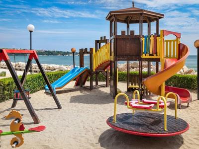 Colorful playground with slides, swing, and merry-go-round on sandy beach under blue sky.